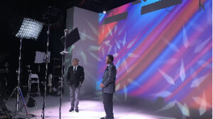 Two black men standing in front of studio white screen with multi colors and lights projected