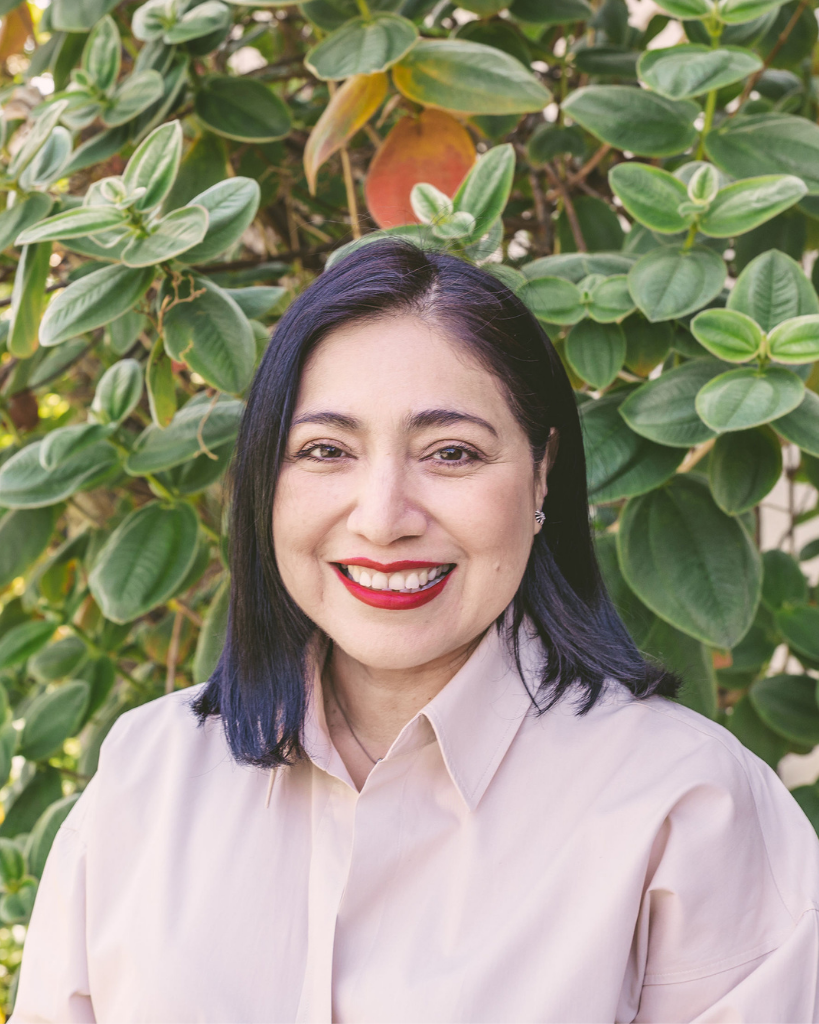 Scatena Daniels Senior Account Executive Geneva Gamez in front of foliage wearing a light tan collared button down top.